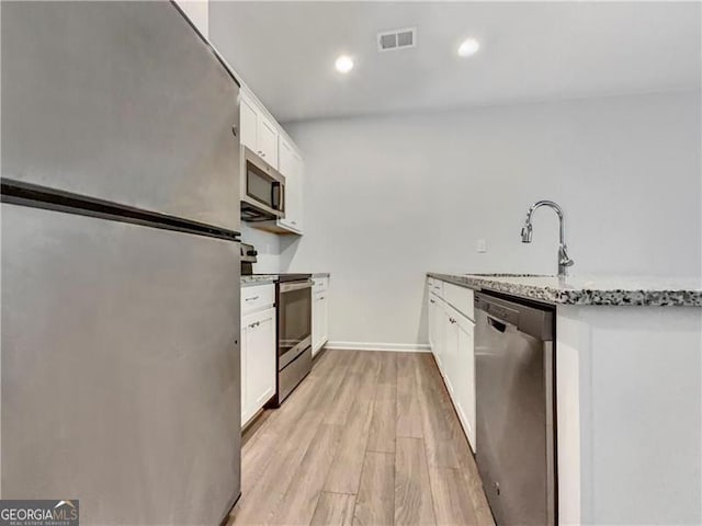 kitchen with sink, stainless steel appliances, light stone counters, light hardwood / wood-style floors, and white cabinets