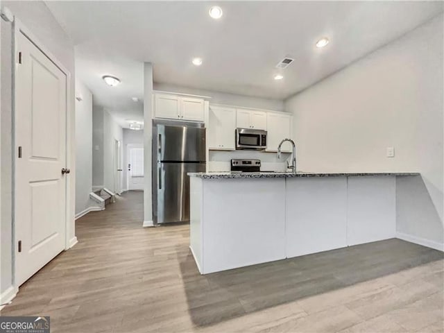 kitchen featuring appliances with stainless steel finishes, light wood-type flooring, white cabinetry, and dark stone counters