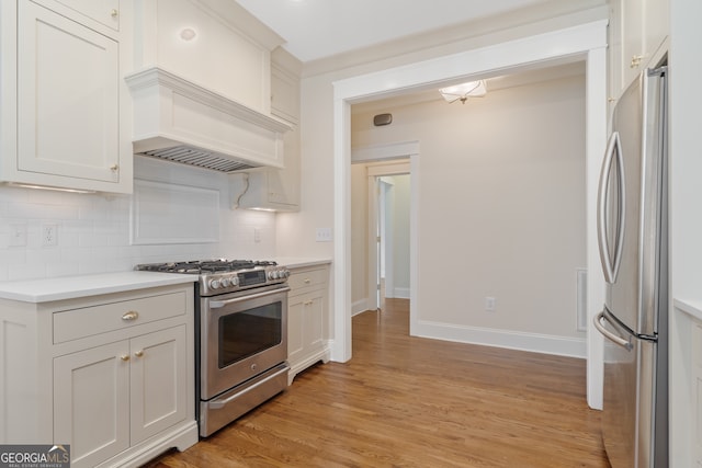 kitchen with backsplash, custom exhaust hood, stainless steel appliances, white cabinets, and light hardwood / wood-style floors