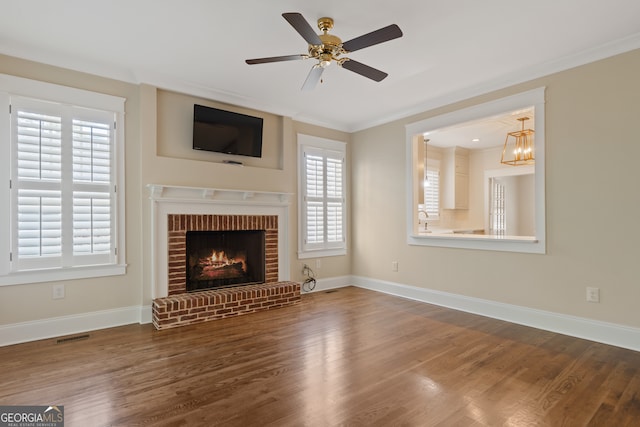 unfurnished living room featuring ceiling fan with notable chandelier, hardwood / wood-style flooring, a brick fireplace, and a wealth of natural light