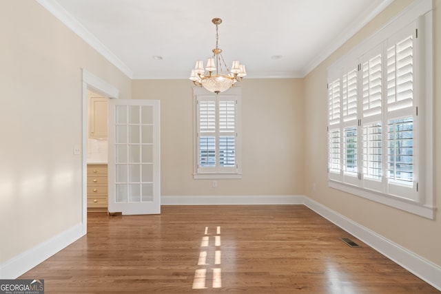 unfurnished dining area with wood-type flooring, crown molding, and a chandelier