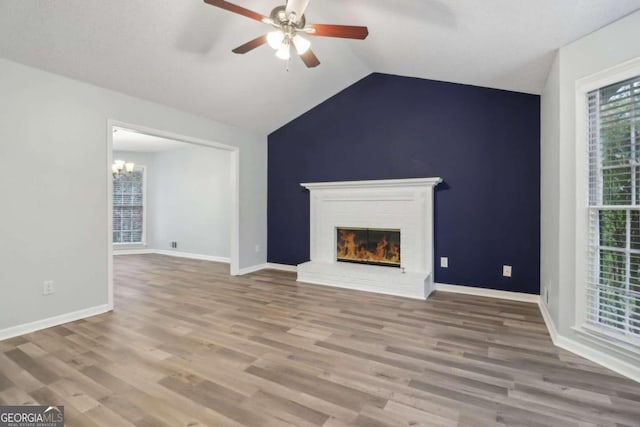 unfurnished living room featuring a fireplace, light hardwood / wood-style flooring, ceiling fan with notable chandelier, and lofted ceiling