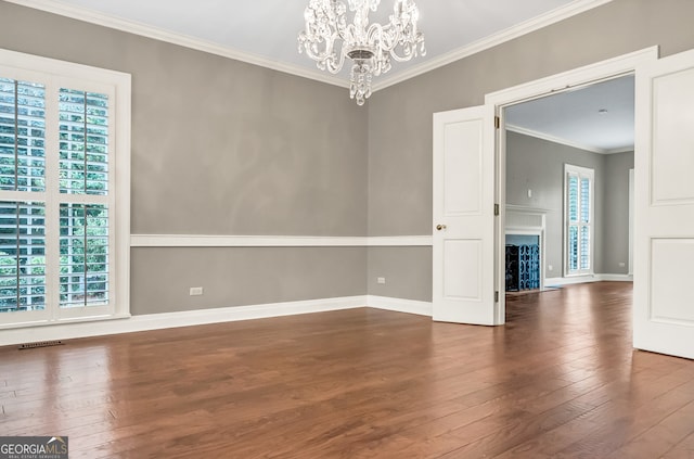 spare room with a chandelier, dark hardwood / wood-style flooring, a wealth of natural light, and ornamental molding