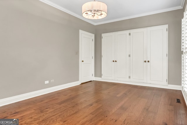 unfurnished bedroom featuring an inviting chandelier, ornamental molding, and hardwood / wood-style flooring