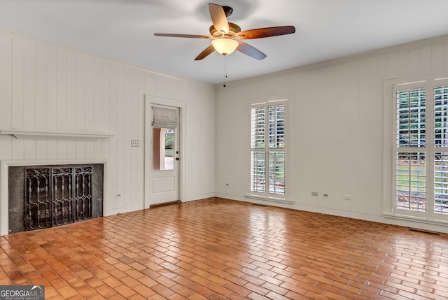 unfurnished living room with ceiling fan and wood walls