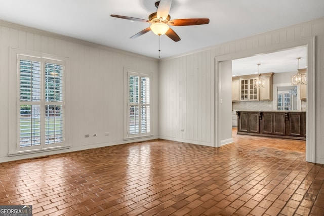 unfurnished living room with wooden walls, a healthy amount of sunlight, and ceiling fan with notable chandelier