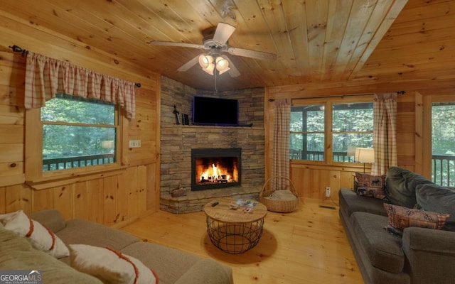 living room featuring wooden walls, a fireplace, ceiling fan, and light hardwood / wood-style floors