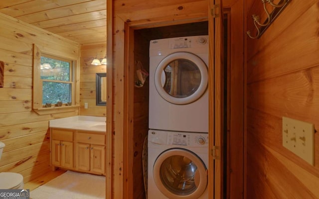 clothes washing area with wooden walls, stacked washing maching and dryer, and wooden ceiling