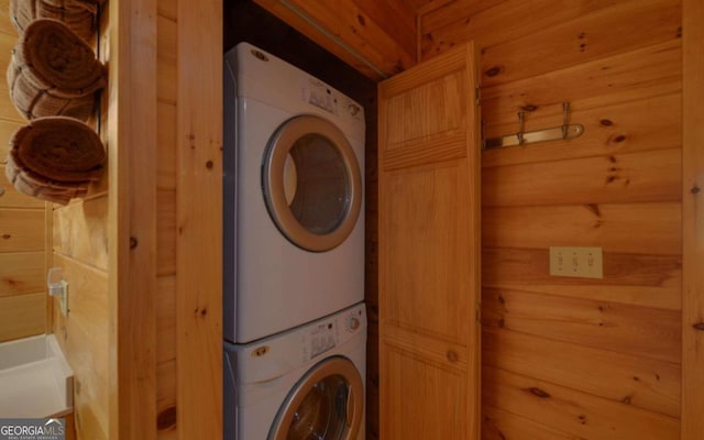 laundry room with stacked washer / drying machine and wood walls