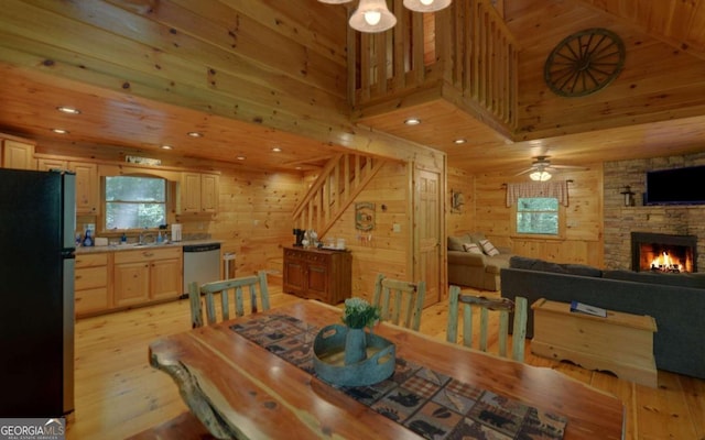 dining space featuring wood walls, a stone fireplace, sink, ceiling fan, and light wood-type flooring