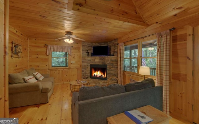 living room featuring wood walls, a stone fireplace, ceiling fan, light hardwood / wood-style floors, and wood ceiling