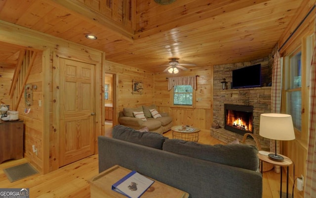 living room with ceiling fan, wooden walls, a fireplace, wood ceiling, and light wood-type flooring