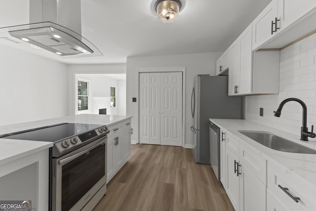 kitchen featuring appliances with stainless steel finishes, wood finished floors, range hood, white cabinetry, and a sink