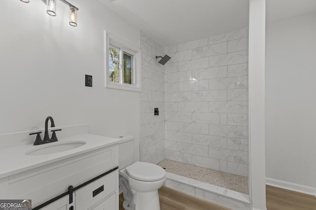 full bath featuring baseboards, tiled shower, toilet, wood finished floors, and vanity