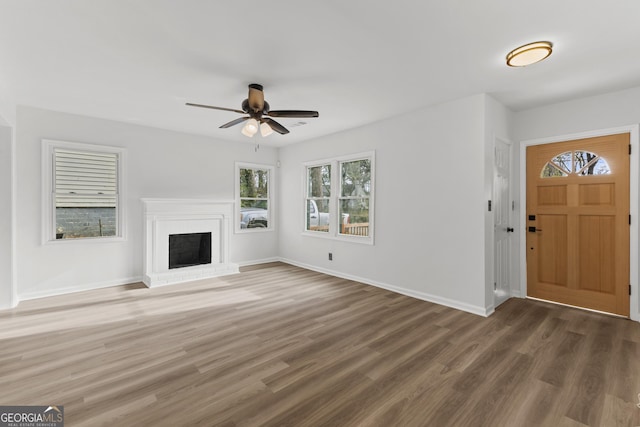 unfurnished living room with a brick fireplace, a ceiling fan, baseboards, and wood finished floors