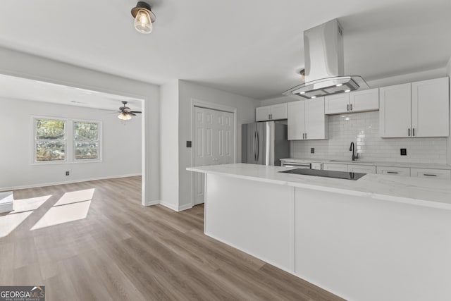 kitchen featuring island range hood, freestanding refrigerator, a sink, light stone countertops, and backsplash