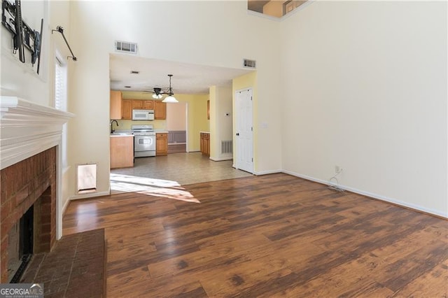 unfurnished living room with dark wood-type flooring, a high ceiling, sink, a brick fireplace, and ceiling fan