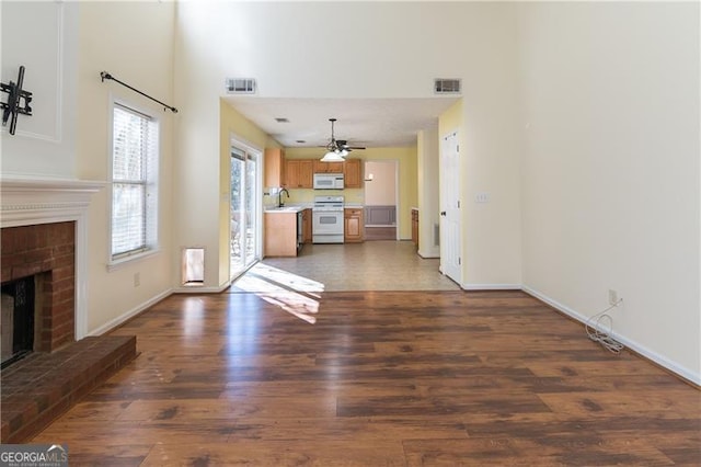 unfurnished living room with ceiling fan, dark hardwood / wood-style flooring, sink, and a brick fireplace