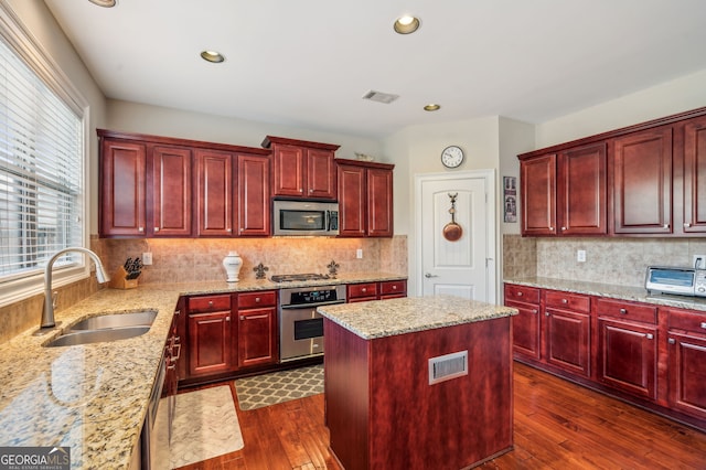 kitchen with light stone countertops, sink, dark hardwood / wood-style flooring, a kitchen island, and appliances with stainless steel finishes