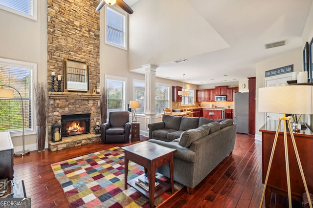 living room featuring a fireplace, ceiling fan, ornate columns, and dark wood-type flooring