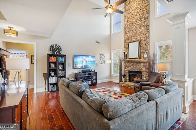 living room featuring a high ceiling, dark hardwood / wood-style flooring, a stone fireplace, and ornate columns