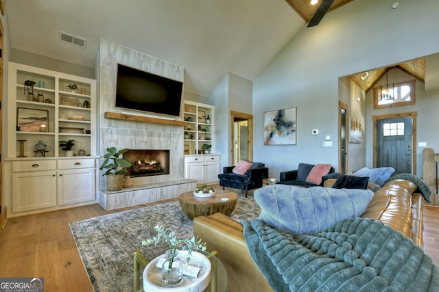 living room featuring beamed ceiling, light hardwood / wood-style floors, a tile fireplace, and high vaulted ceiling