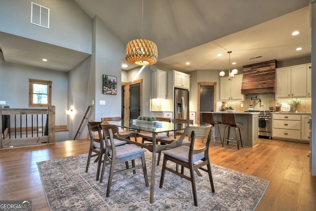 dining space featuring light wood-type flooring, high vaulted ceiling, and a notable chandelier