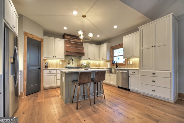 kitchen featuring a kitchen island, light hardwood / wood-style flooring, decorative light fixtures, white cabinets, and appliances with stainless steel finishes