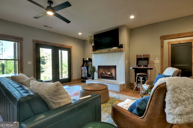 living room with a tiled fireplace, ceiling fan, french doors, and light hardwood / wood-style floors