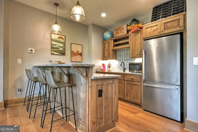 kitchen featuring appliances with stainless steel finishes, light hardwood / wood-style floors, decorative light fixtures, and a kitchen breakfast bar