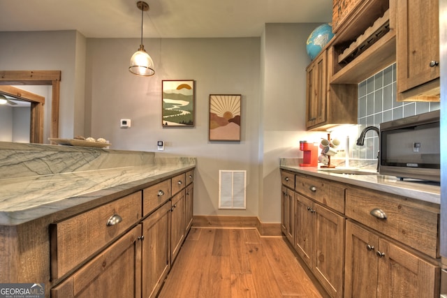 kitchen featuring pendant lighting, decorative backsplash, light wood-type flooring, and sink