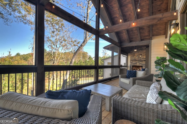 sunroom / solarium with lofted ceiling with beams, a stone fireplace, and wooden ceiling