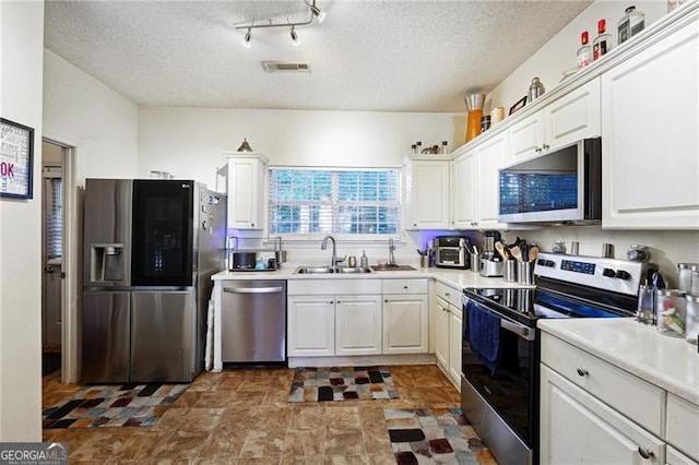 kitchen featuring white cabinetry, sink, rail lighting, a textured ceiling, and appliances with stainless steel finishes