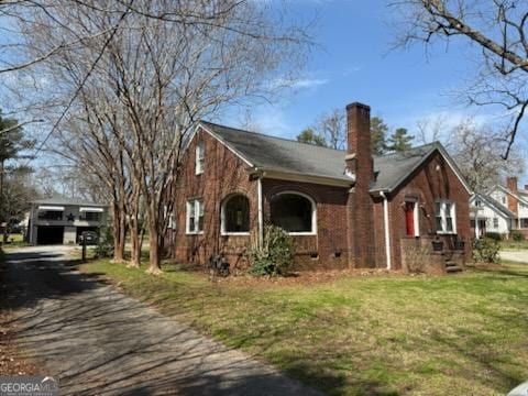 view of front facade with aphalt driveway, a chimney, and a front yard