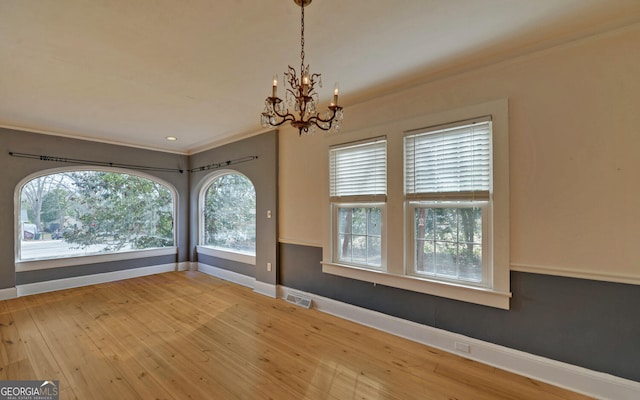 empty room with ornamental molding, wood-type flooring, and a chandelier