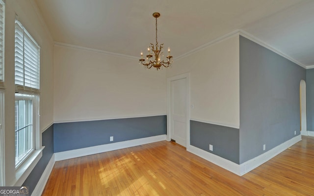 empty room with crown molding, hardwood / wood-style floors, and an inviting chandelier