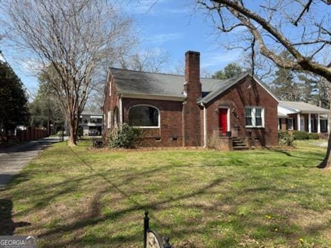 view of front of home featuring brick siding, a chimney, and a front lawn