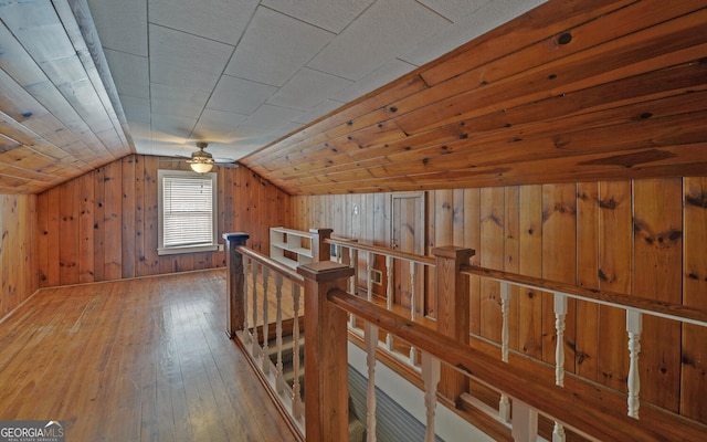 hallway featuring wood-type flooring, wood walls, and vaulted ceiling