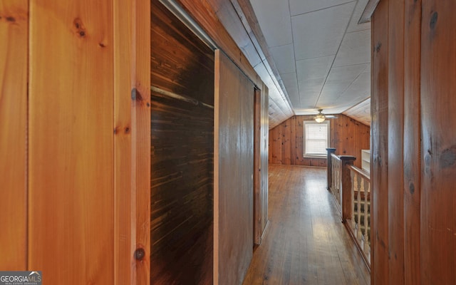 hall with vaulted ceiling, hardwood / wood-style floors, and wood walls