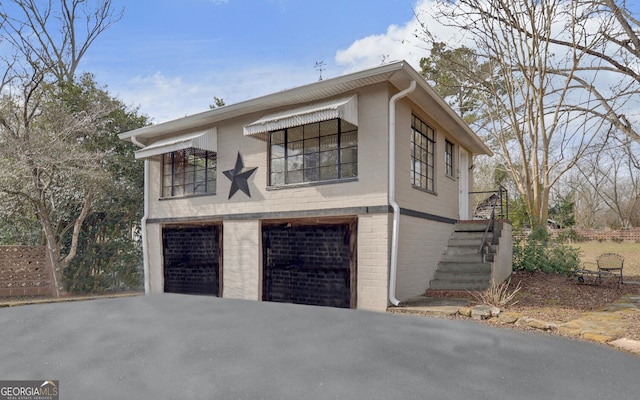 view of home's exterior with a garage, brick siding, stairway, and aphalt driveway