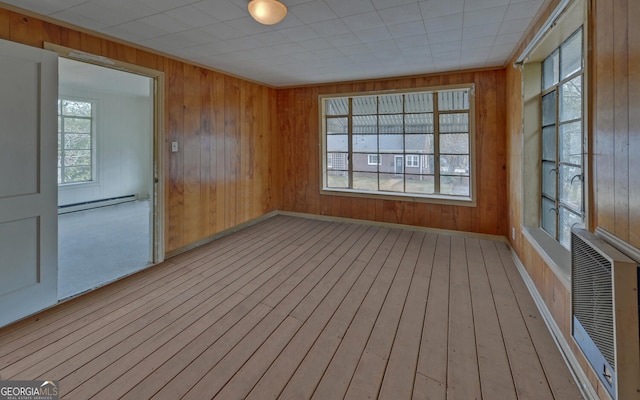 empty room featuring plenty of natural light, wooden walls, baseboard heating, and light hardwood / wood-style flooring