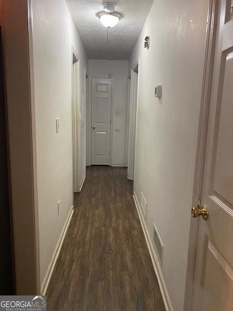 corridor with dark hardwood / wood-style floors and a textured ceiling