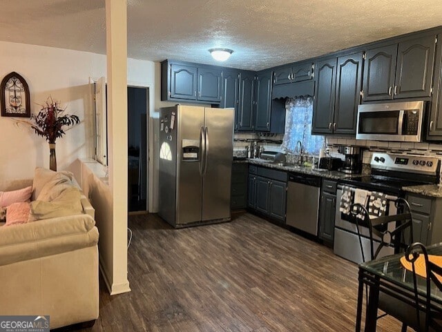 kitchen featuring sink, dark hardwood / wood-style flooring, dark stone countertops, a textured ceiling, and appliances with stainless steel finishes