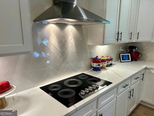 kitchen featuring tasteful backsplash, black electric cooktop, white cabinetry, and wall chimney exhaust hood