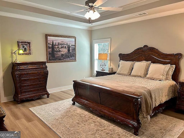 bedroom featuring light wood-type flooring, a raised ceiling, ceiling fan, and crown molding