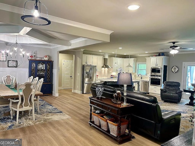 living room with ceiling fan with notable chandelier, light hardwood / wood-style flooring, and crown molding