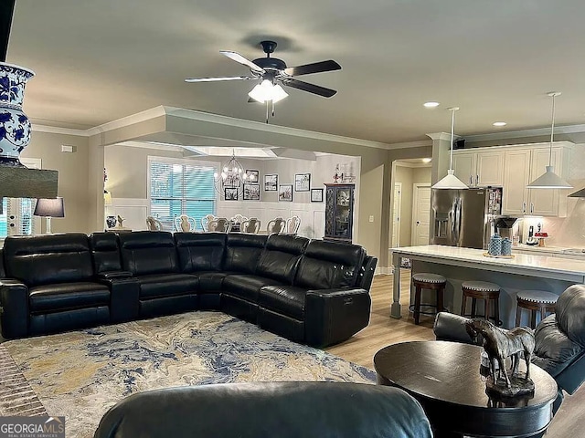 living room featuring ceiling fan with notable chandelier, light hardwood / wood-style floors, and ornamental molding