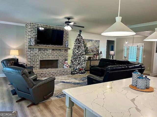 living room with a brick fireplace, ceiling fan, hardwood / wood-style floors, and ornamental molding