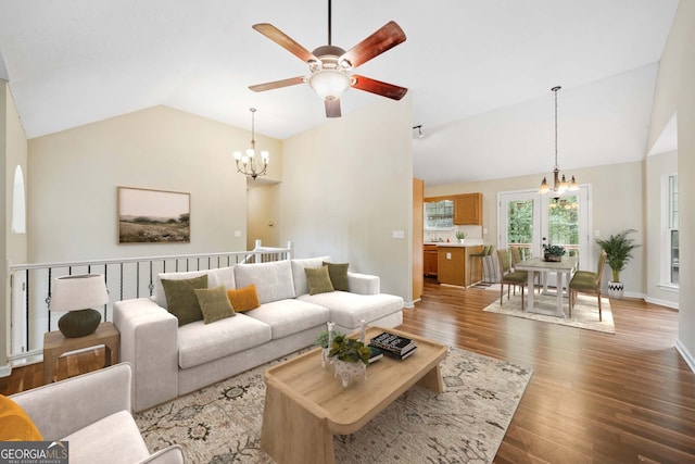 living room with ceiling fan with notable chandelier, hardwood / wood-style flooring, and vaulted ceiling