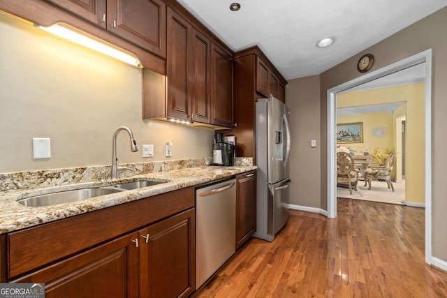 kitchen with appliances with stainless steel finishes, light hardwood / wood-style floors, light stone counters, and sink